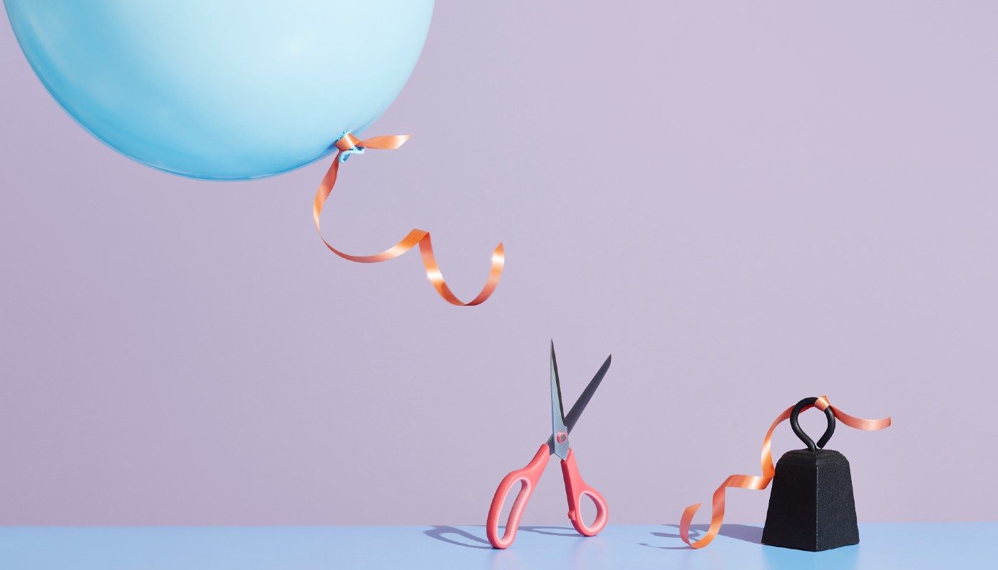 String connecting a balloon and weight is cut with scissors to represent the sunk cost fallacycissors