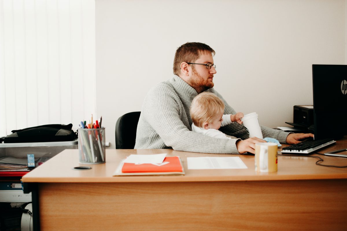 Image of a dad working on a computer with a toddler on his lap