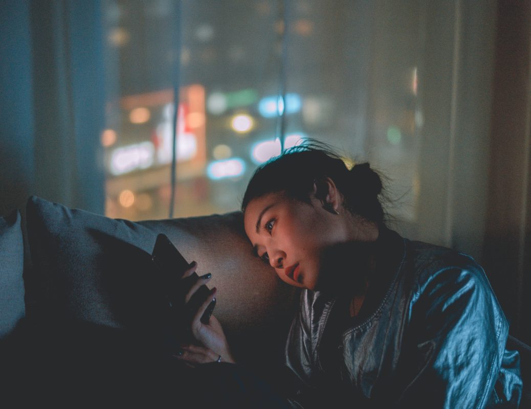 Image of a young woman in a dark room by herself starring at her mobile phone