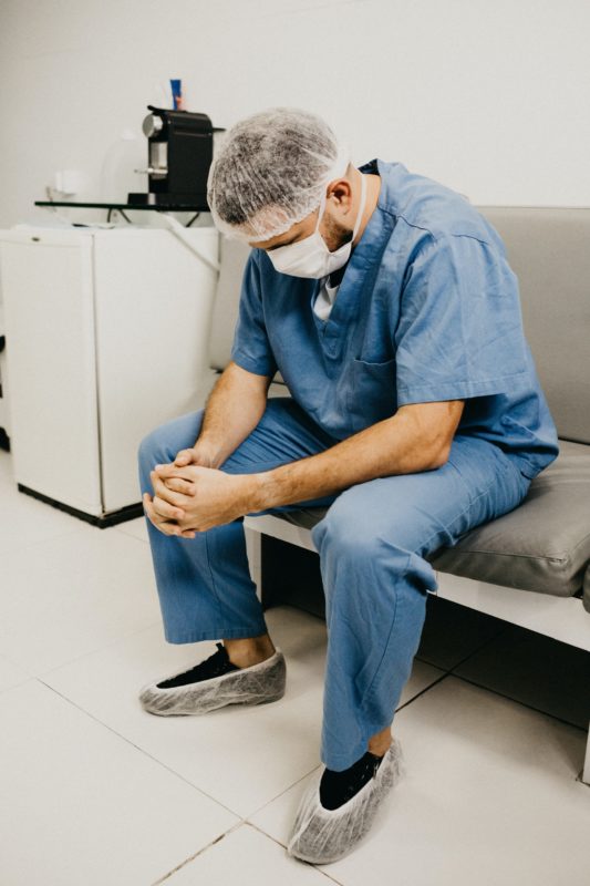 Image of a tired looking male nurse looking at the floor